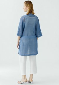 Himmelblauer, luftiger Kimono mit Dreiviertelärmeln, tailliertem Gürtel und seitlichen Schlitzen, kombiniert mit weißen, verkürzten Hosen und silbernen Sandalen.