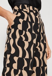 Höga byxor med ett geometriskt mönster i svart och beige. Tillverkade av lätt tyg, med sidofickor och resår i midjan.