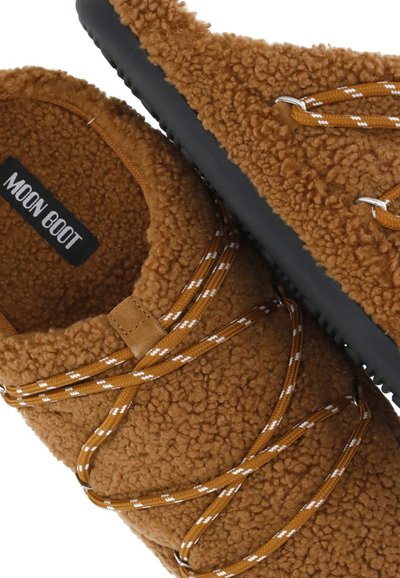 Chaussures à enfiler marron à peluche avec semelles noires et lacets marron avec accents blancs, marquées "MOON BOOT" à l'intérieur du talon.