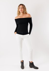 Top nero scollato sulle spalle con maniche lunghe e tessuto arricciato. Abbinato a pantaloni bianchi a taglio slim e stivali neri alla caviglia con zip laterale.
