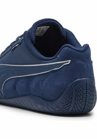 Chaussure de sport bleu marine avec une tige en cuir lisse et des accents en daim, une semelle en caoutchouc texturée et des détails réfléchissants sur le côté.