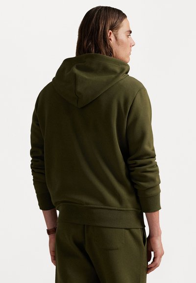 Ελαιοπράσινη κουκούλα φούτερ κατασκευασμένη από μαλακό ύφασμα, με καγκουρό τσέπη, ριμπ μανσέτες και χαλαρή εφαρμογή. Ορατή υφή και ραφές.