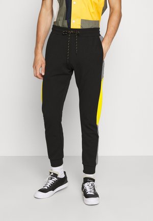 Zwarte joggingbroek met een trekkoord in de tailleband, voorzien van gele en grijze zijpanelen. Gemaakt van zachte stof met geribde boorden.