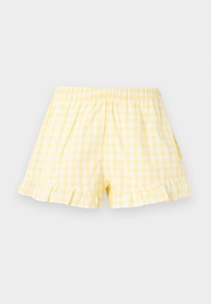 Pantaloni scurți cu talie elastică, cu model gingham alb și galben și tivuri cu volănașe, expuși pe un fundal simplu și deschis la culoare.
