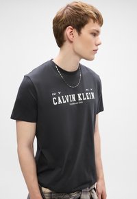 Musta lühikeste varrukatega t-särk, millel on valge "CALVIN KLEIN" logo. Sile puuvillane materjal, ümar kaelus ja mugav lõige. Kandmiseks on lisatud helkkäevõru.