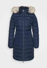 Navy blauw pufferjack met een nepbontkap, gequilt ontwerp, vooraan met ritssluiting en zijzakken. Zachte textuur en slanke silhouet.