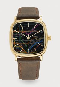 Reloj cuadrado con caja de tono dorado, esfera con mapa de metro en negro, índices horarios en blanco y correa de cuero marrón con costura visible.