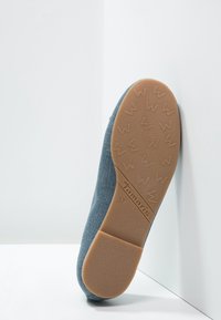 Blå textilskosula med en strukturerad brun gummibas, som har en logo och storlek. Formen är något rundad vid tån.