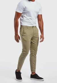 Khaki chinos w slimowanym kroju, z bocznymi kieszeniami, zapięciem na guzik oraz zamkiem na kostce, w połączeniu z czarnymi sneakerami.