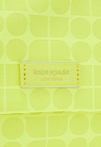 Tessuto di nylon giallo con motivi circolari in rilievo. Presenta un'etichetta cucita con la scritta "kate spade NEW YORK" attaccata in un colore giallo coordinato.