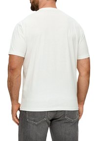 Biała bawełniana koszulka z krótkim rękawem i okrągłym dekoltem, pokazana z tyłu. Para szarych dżinsów z widocznymi tylnymi kieszeniami.