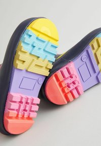 Semelles de chaussures avec des motifs de semelles multicolores en jaune, bleu, violet, rose et rouge sur un fond clair.