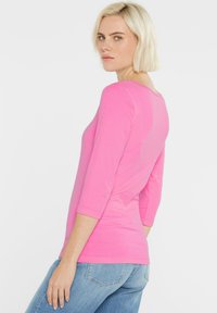 Rosa Langarmshirt mit Rundhalsausschnitt und gerippten Abschlüssen. Weicher Stoff mit tailliertem Design, kombiniert mit blauen Jeans.
