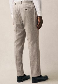 Pantalones ajustados de color gris claro con un acabado texturizado, detalle de pliegue y dos bolsillos traseros. Combinados con mocasines negros, que muestran un corte limpio.