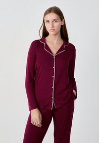 Ensemble de pyjama bourgogne avec manches longues, passepoil blanc et fermeture à bouton. Tissu doux, coupe décontractée, avec poches sur le pantalon.