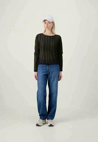 Fekete kötött pulóver hosszú ujjakkal, laza, kék farmernadrággal és szürke sportcipővel párosítva. A modellen fehér baseballsapka van.