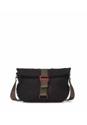 Persona con suéter marrón y pantalones marrones de pierna ancha, llevando un bolso bandolera negro con correa beige y hebilla roja.