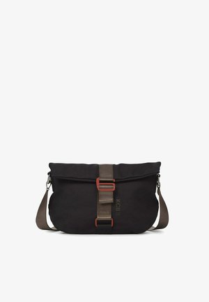 Persona con suéter marrón y pantalones marrones de pierna ancha, llevando un bolso bandolera negro con correa beige y hebilla roja.