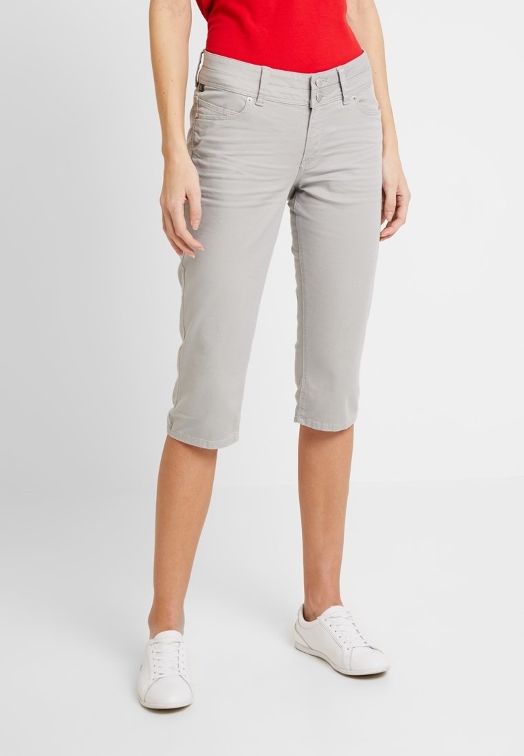 Pantalones capri gris claro de mezcla de algodón, con cierre frontal de botón, cinco bolsillos y un ajuste relajado, combinados con zapatillas blancas.