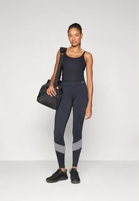 Svart tanktopp, mørke leggings med grå aksentstriper, svarte joggesko og en svart veske. Strømlinjeformet design, tettsittende form og glatt tekstur.