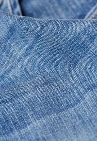 Denim-kangas vaaleansinisenä, jossa on sileä pinta, hienovarainen vinokudontamalli ja pieniä vaihteluita väriintensiteetissä.