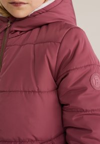 Bordo puffer jakna s sjajnom, glatkom teksturom; ima kapuljaču, zlatni patentni zatvarač i okrugli logotip na lijevom rukavu.