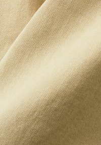 Tela beige con una sutil textura acanalada, que muestra una superficie lisa y un ligero brillo, enfatizando su estructura tejida y la consistencia del color.