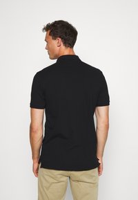 Camisa polo negra de manga corta, hecha de algodón. Tiene cuello tipo polo y un dobladillo recto. Se lleva con pantalones caqui de color claro.