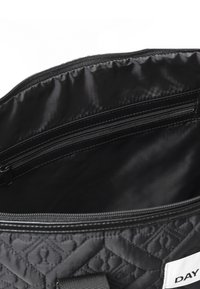 Svart vadderad väskinsida med slät yta, har en dragkedjeficka och en tygetikett med texten "DAY" på sidan.