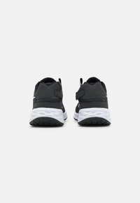 Scarpe sportive nere con una tomaia liscia e una suola intermedia bianca, dotate di una fascia in velcro e suola esterna nera testurizzata per una migliore aderenza.