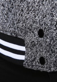 Grå tekstureret stof med en fuzzy udseende, med sorte knapper og en sort ribbet kant med hvide striber.