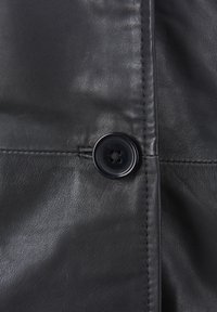 Zwarte leren kleding met een gladde textuur, voorzien van een ronde zwarte knop en zichtbare stiksels langs de randen. Geen patronen of logo's.