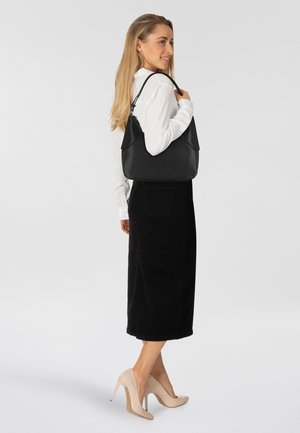 Borsa a tracolla in pelle nera con una forma morbida e parte superiore ripiegata. Indossata sulla spalla, abbinata a una camicia bianca e una gonna nera.