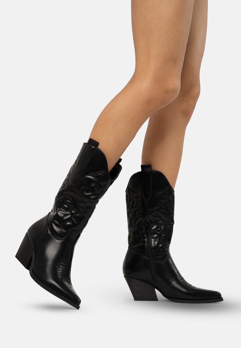 Botas de cowboy de cuero negro con puntas afiladas, diseños bordados, un tacón de altura media y cremalleras laterales para facilitar su uso.