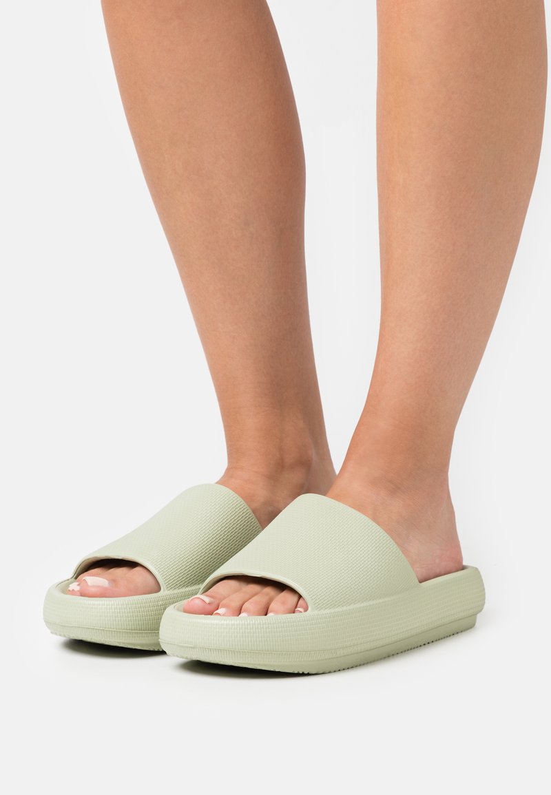 Sandale de cauciuc de culoare verde deschis, cu un design texturat, vârful deschis și talpa groasă, cu pernuțe de amortizare.