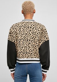 Džemper s uzorkom leoparda i crnim rukavima, rebraste manžete u bijeloj i crnoj prugastoj kombinaciji. Skraćen dizajn, mekana tekstura.
