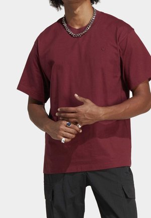 Personne portant un t-shirt bordeaux, un pantalon cargo noir, un collier chaîne argentée et plusieurs bagues en argent aux mains.