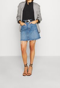 Jeanskjolen har en fransad fåll och är kombinerad med en svart blus och en grå rutig blazer. Svart strappy heels fulländar looken.