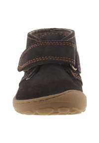 Zwarte suède schoenen met oranje stiksels, klittenbandsluiting, ronde neus en rubberen zool, uitgerust met een gestructureerd grippatroon aan de onderkant.