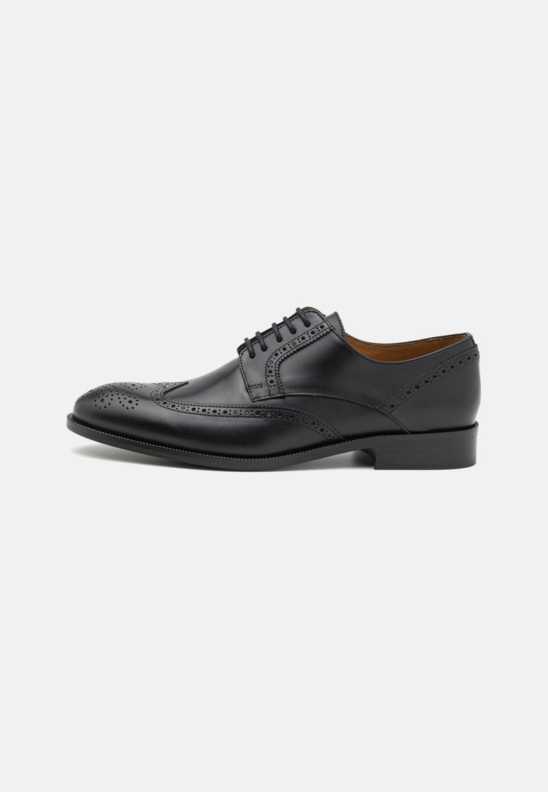 Chaussure habillée en cuir noir avec des détails de perforation, embout rond, design à lacets à cinq œillets et un léger talon rehaussé. Texture lisse.