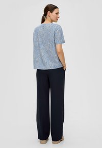 Haut bleu à motifs avec des manches courtes, associé à un pantalon noir ample. Le haut présente un design texturé et un détail de fermeture dans le dos.