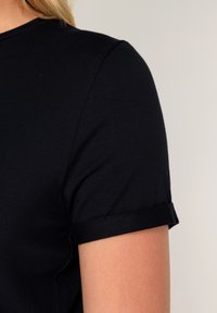 Zwart katoenen T-shirt met ronde hals en korte mouwen. De mouwen zijn opgerold, wat de gladde stoftextuur benadrukt.