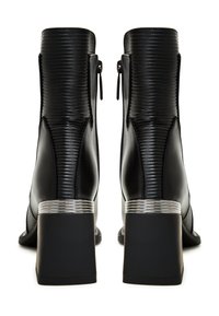 Zwarte leren enkelbotten met een gestructureerd verticaal patroon, achterritsen en een brede blokhak met een zilverkleurig accent.