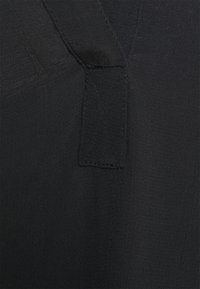 Schwarzer Stoff mit strukturierter Oberfläche, bestehend aus einem genähten Patch und diagonalen Nähdetails. Glatte und leicht glänzende Optik.