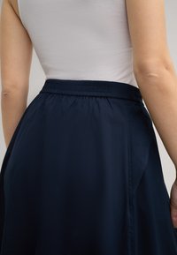 Marineblauer Rock mit einem elastischen Bund, der eine glatte Textur und eine A-Linien-Form aufweist. Das Design ist simpel, ohne sichtbare Muster oder Akzente.