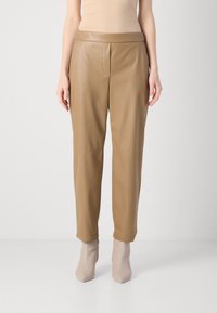 Tan leren broeken met een gladde textuur, met een hoge taille, zijzakken en taps toelopende pijpen, gecombineerd met lichtbeige hoge hakken.