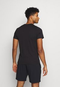 Svart kortermet t-skjorte laget av bomull, med klassisk rund hals og slim fit-design, iført med mørke shorts, sett bakfra.