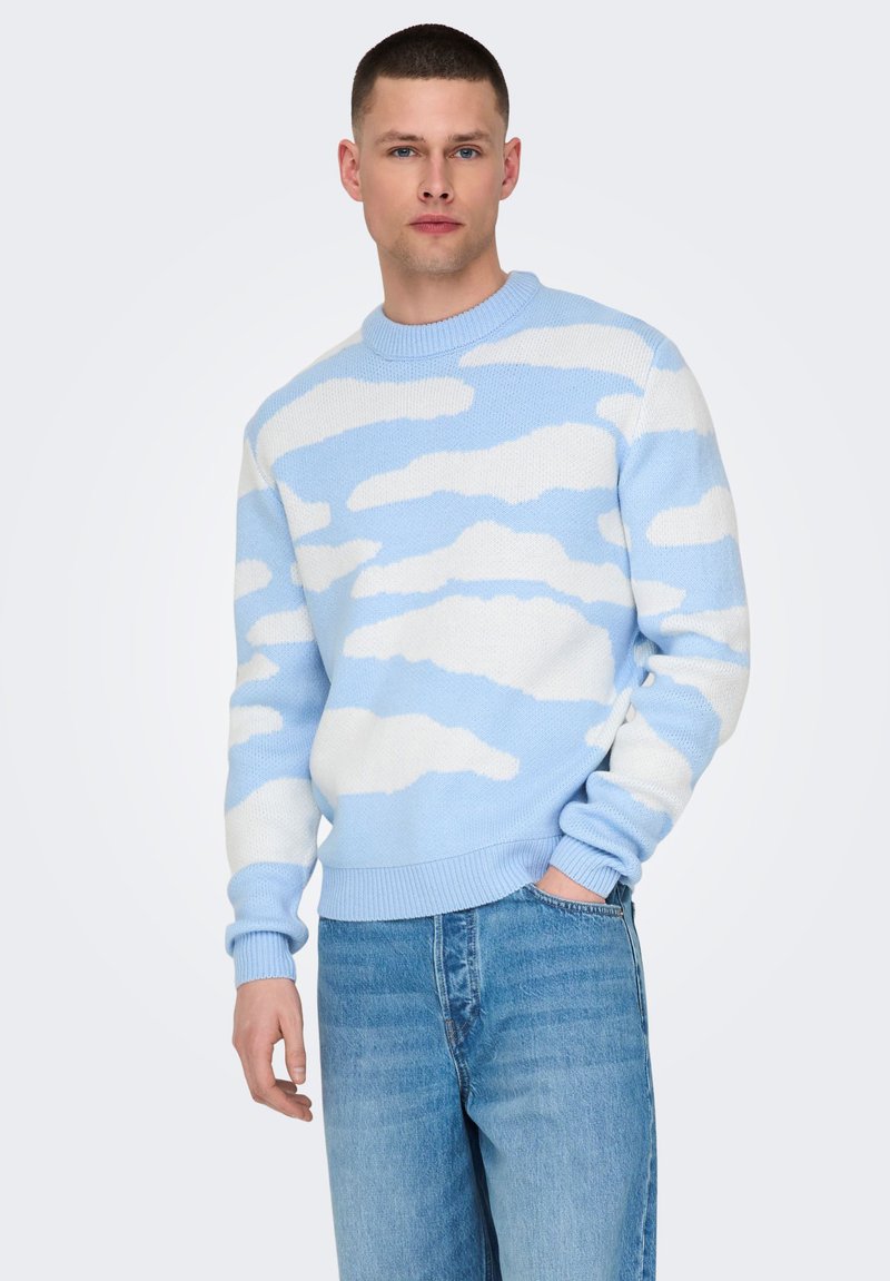 Lyseblå strikket sweater med hvide skymønstre, rund halsudskæring og ribbede manchetter, parret med lyseblå denimjeans.