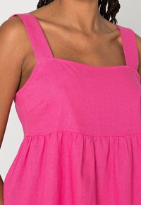 Robe rose sans manches avec un col carré, une taille froncée et une texture lisse en lin. Comprend un petit détail de poche latérale.