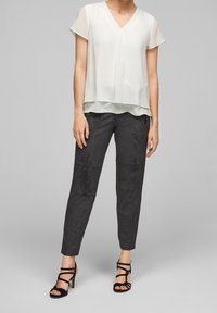 Blusa leggera in crema con maniche corte e scollo a V, abbinata a pantaloni grigio scuro con texture e tacchi neri con cinturini.